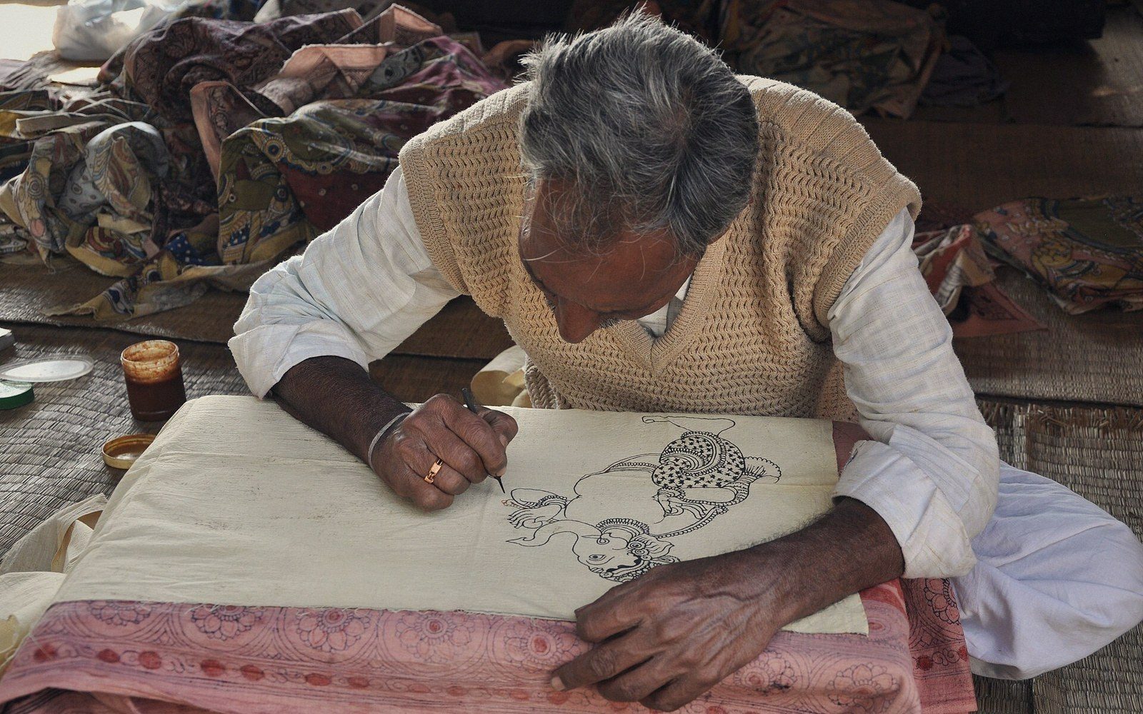 Artisan hand-draws a kalamkari design in ink on fabric