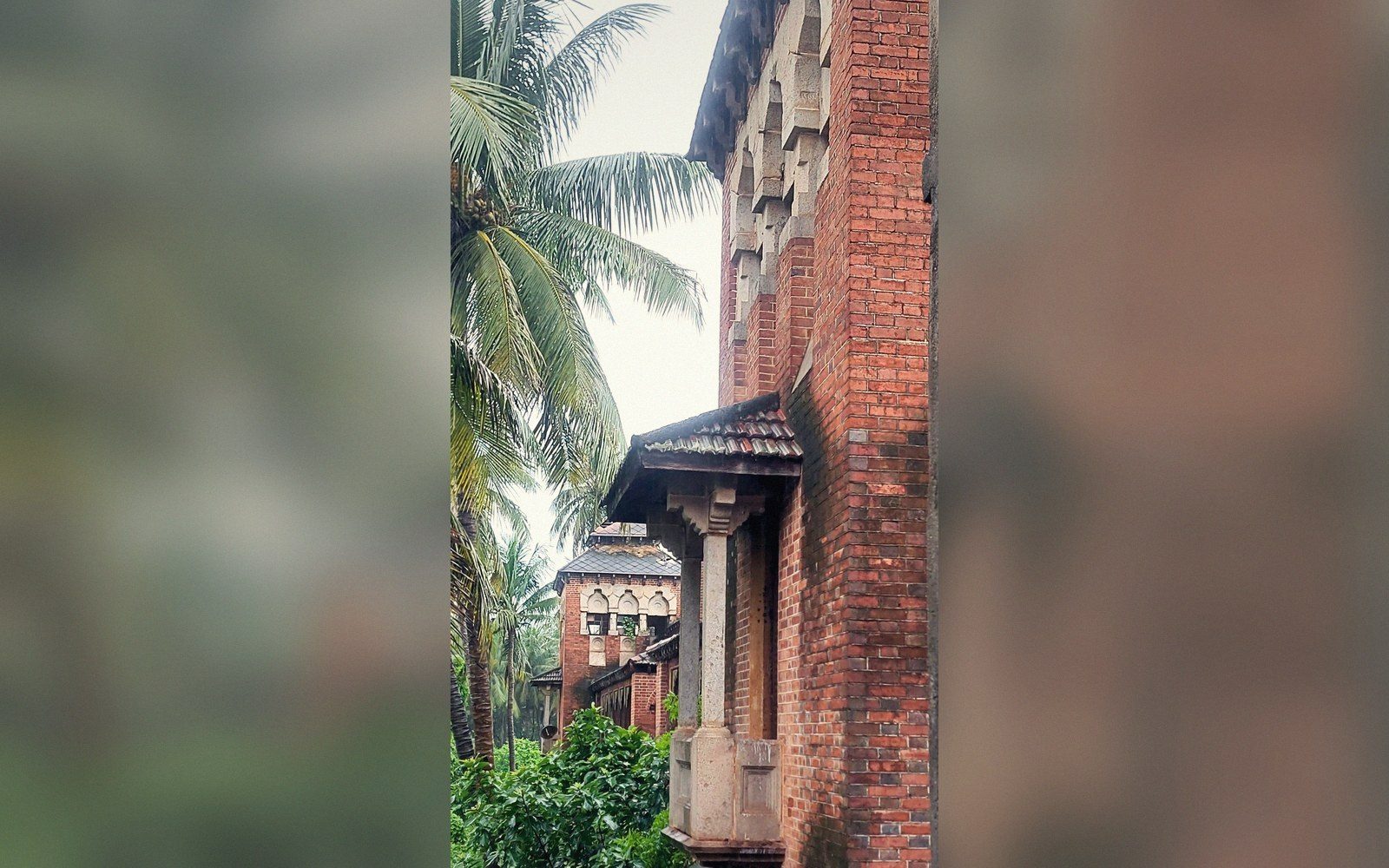 Weathered brick tower with carved stone pillar and tiled roof among palm trees
