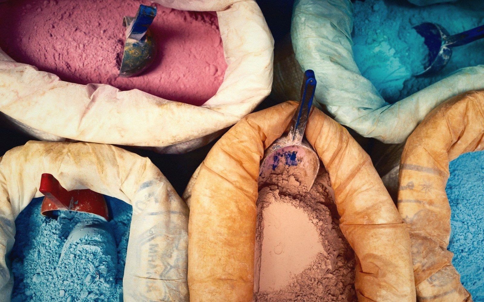 Sacks of colored dye powders with scoops resting in pink, blue, orange and gray pigments