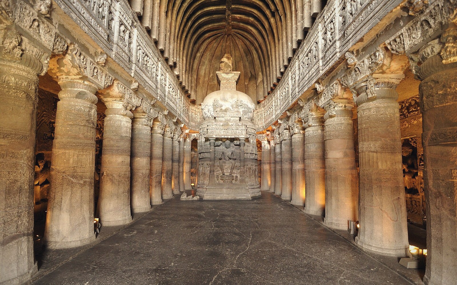 Carved stone stupa flanked by rows of pillars inside a vaulted rock-cut cave hall